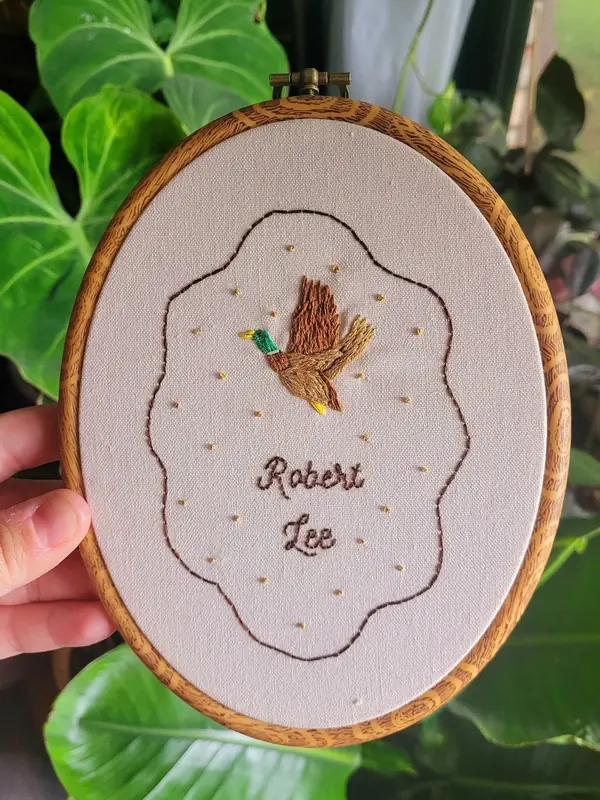 Embroidery hoop with a mallard in flight and the name Robert Lee