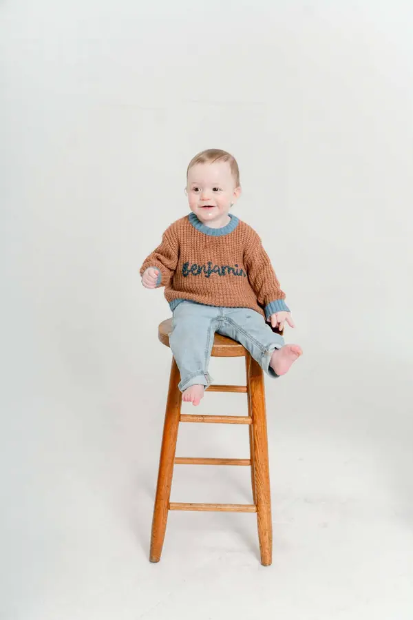 Toddler sitting on a stool in a name-embroidered sweater