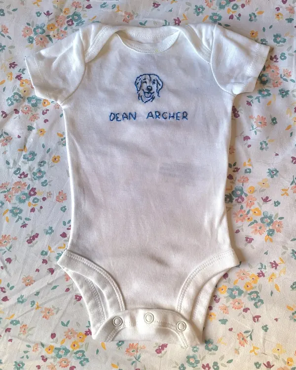 Baby onesie embroidered with a dog and the name Dean Archer