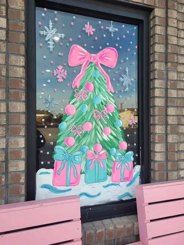 Window painted with a pastel pink Christmas tree and presents